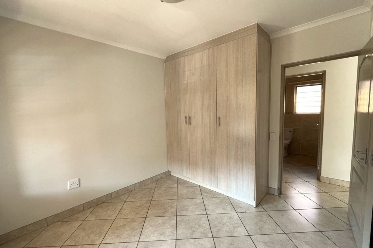 A bedroom featuring built-in wooden cabinetry, tiled flooring, and an adjoining en-suite bathroom.