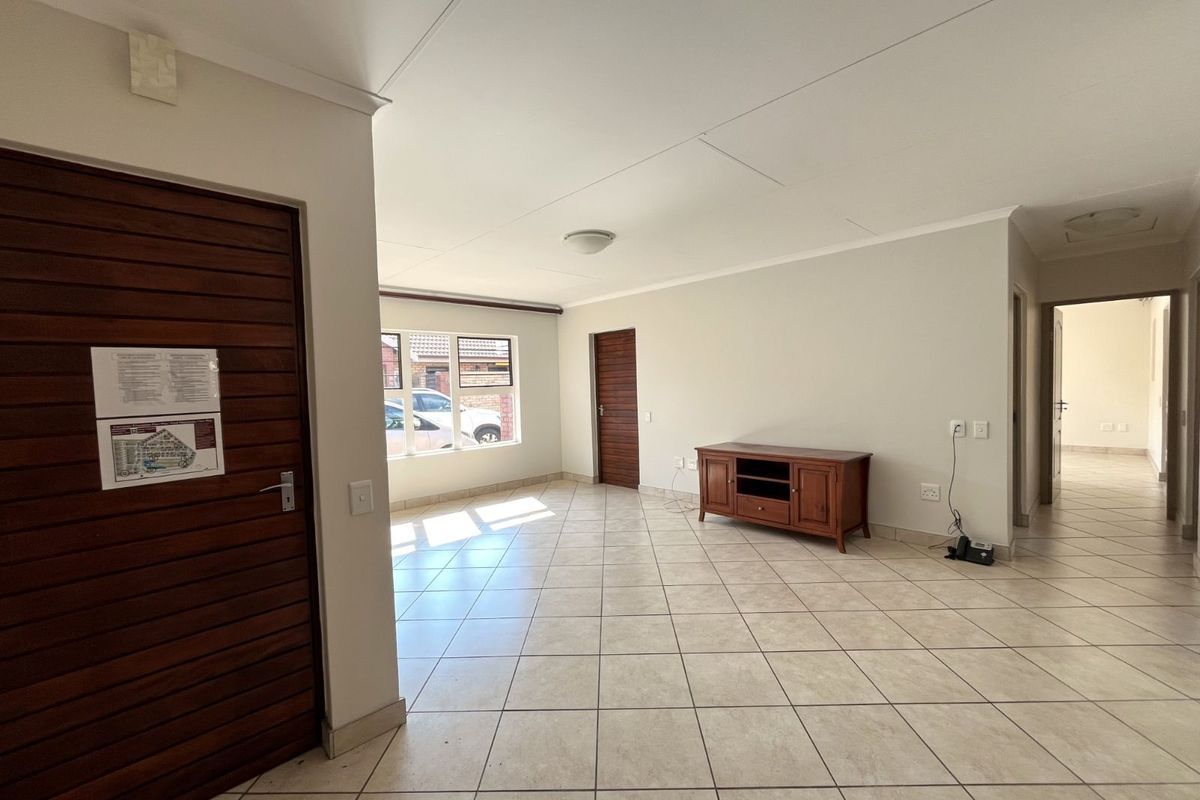 Spacious open-plan living area featuring neutral tiled flooring, clean white walls, and wooden interior doors, offering a bright and versatile living space.