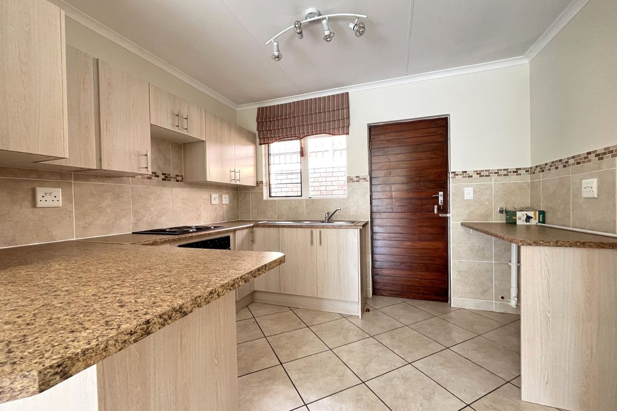 A functional kitchen featuring light wood-grain cabinetry, granite-look countertops, tiled splashbacks, and a built-in hob, with direct access to an exterior door.