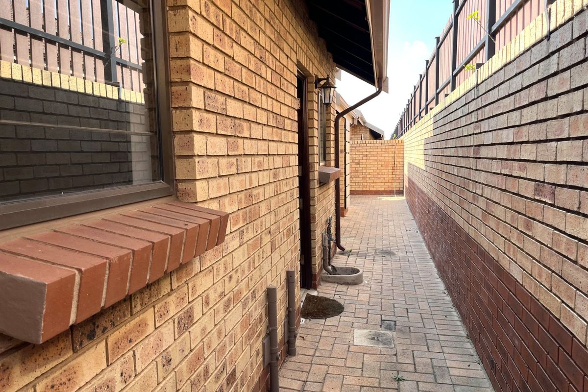 A side exterior walkway featuring face-brick walls, paved flooring, and a secure boundary fence, providing access along the side of the townhouse.