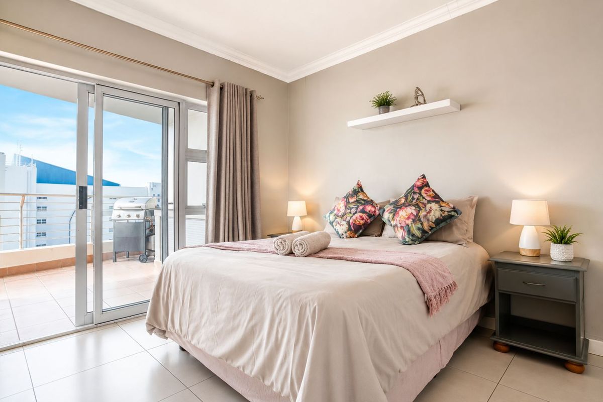 A well-maintained bedroom featuring tiled flooring, crown molding, and large sliding glass doors that open onto a private balcony.