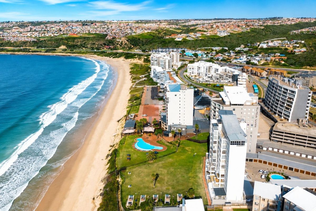 Aerial view of a coastal residential complex featuring a swimming pool, landscaped grounds, and direct access to the beach.