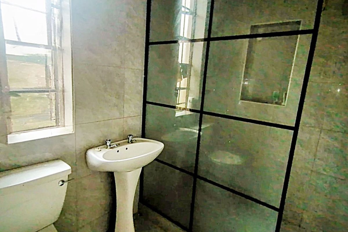 A functional bathroom featuring a pedestal basin, toilet, and a framed glass shower enclosure with tiled walls.