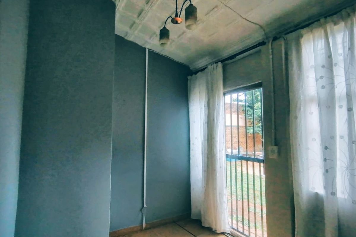 A small interior room featuring a metal security gate leading to the exterior, surface-mounted electrical wiring, and a textured ceiling finish.