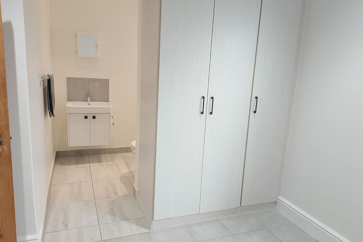 A clean, modern bedroom featuring built-in wardrobes and an en-suite bathroom with a vanity basin and tiled flooring.