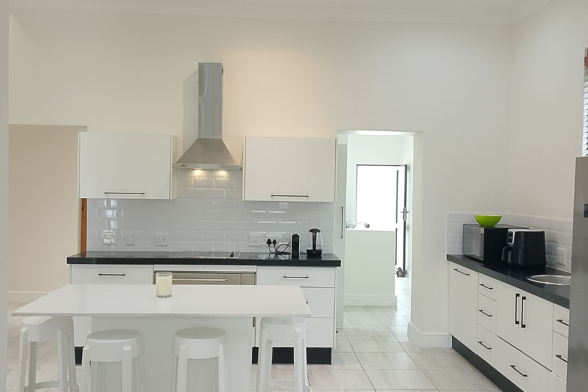 Modern kitchen featuring white cabinetry, contrasting black countertops, a central island, stainless steel extractor fan, and tiled flooring with recessed ceiling lighting.