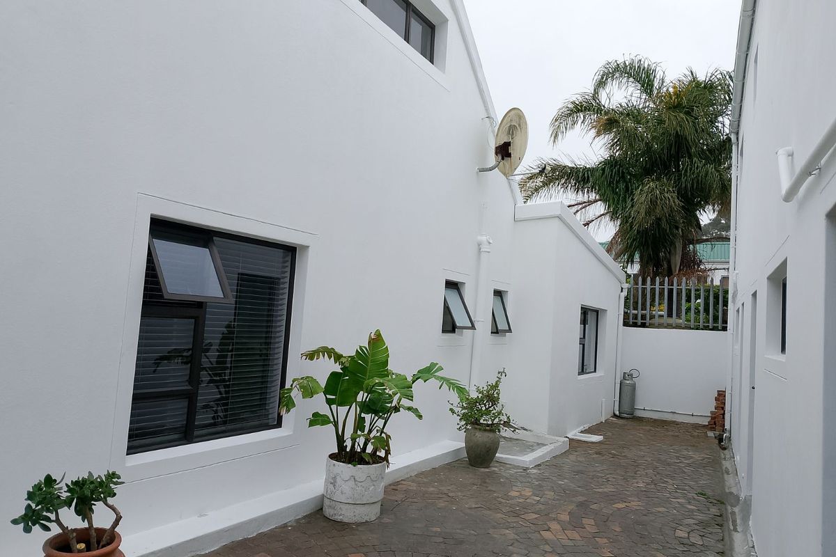 A side exterior view of the property featuring white rendered walls, dark-framed windows, and paved ground area.