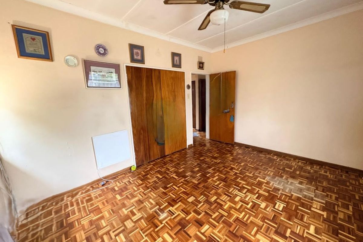 A bedroom featuring classic parquet flooring, built-in wooden wardrobes, and a ceiling fan, offering a functional space with potential for cosmetic updates.