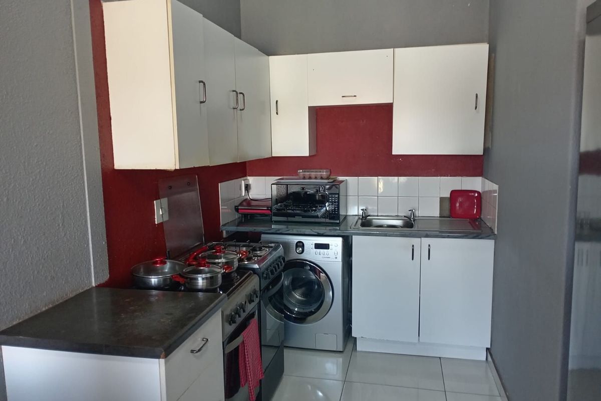 Compact kitchen featuring white cabinetry, tiled splashback, integrated stove, and space for a front-loading washing machine.