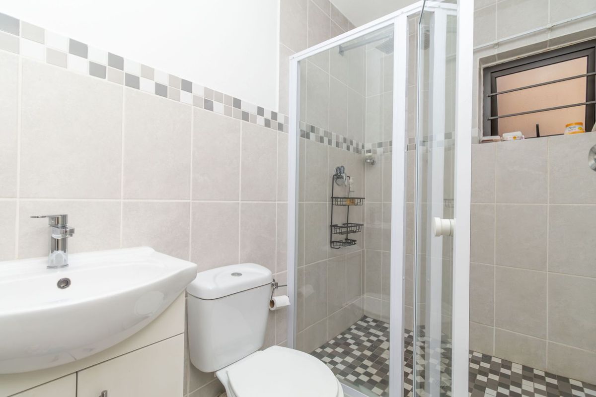 A clean, modern bathroom featuring a glass-enclosed shower, a pedestal vanity basin, and a toilet with neutral wall tiling and patterned floor tiles.