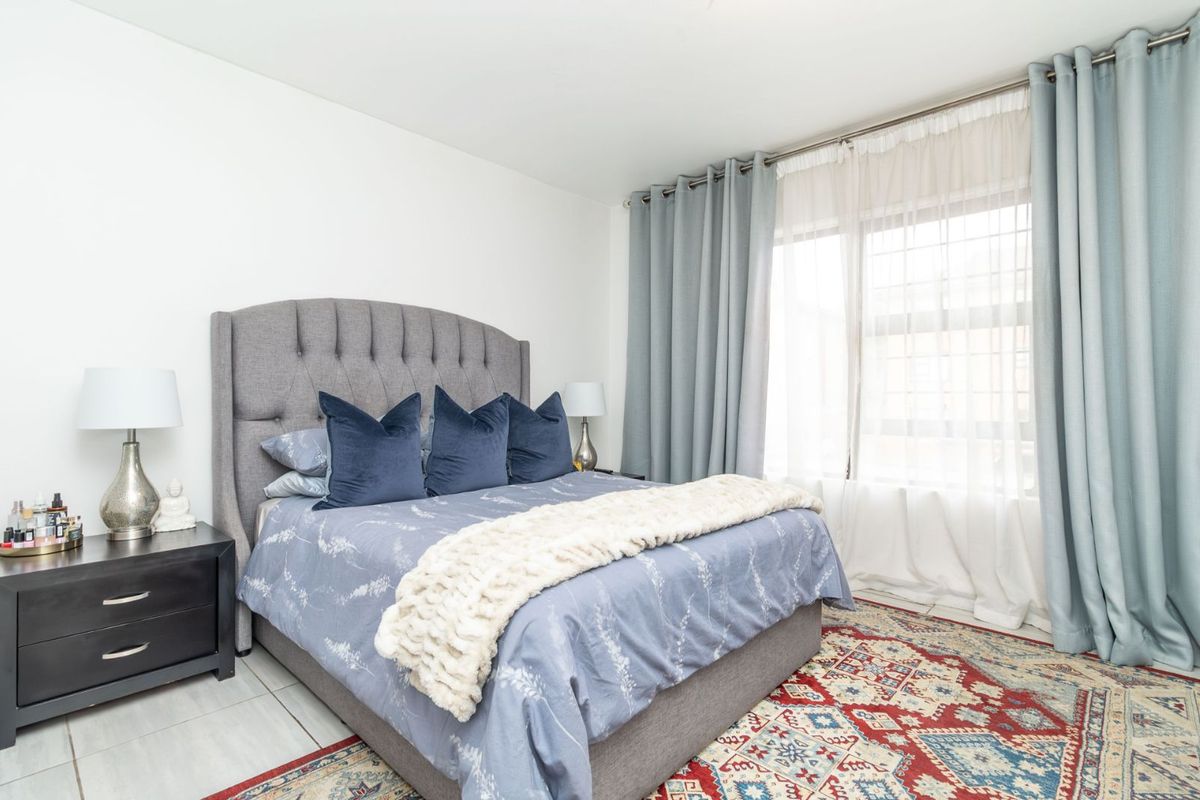 A well-lit bedroom featuring neutral walls, tiled flooring, and large windows with floor-to-ceiling curtains, providing a comfortable and bright living space.