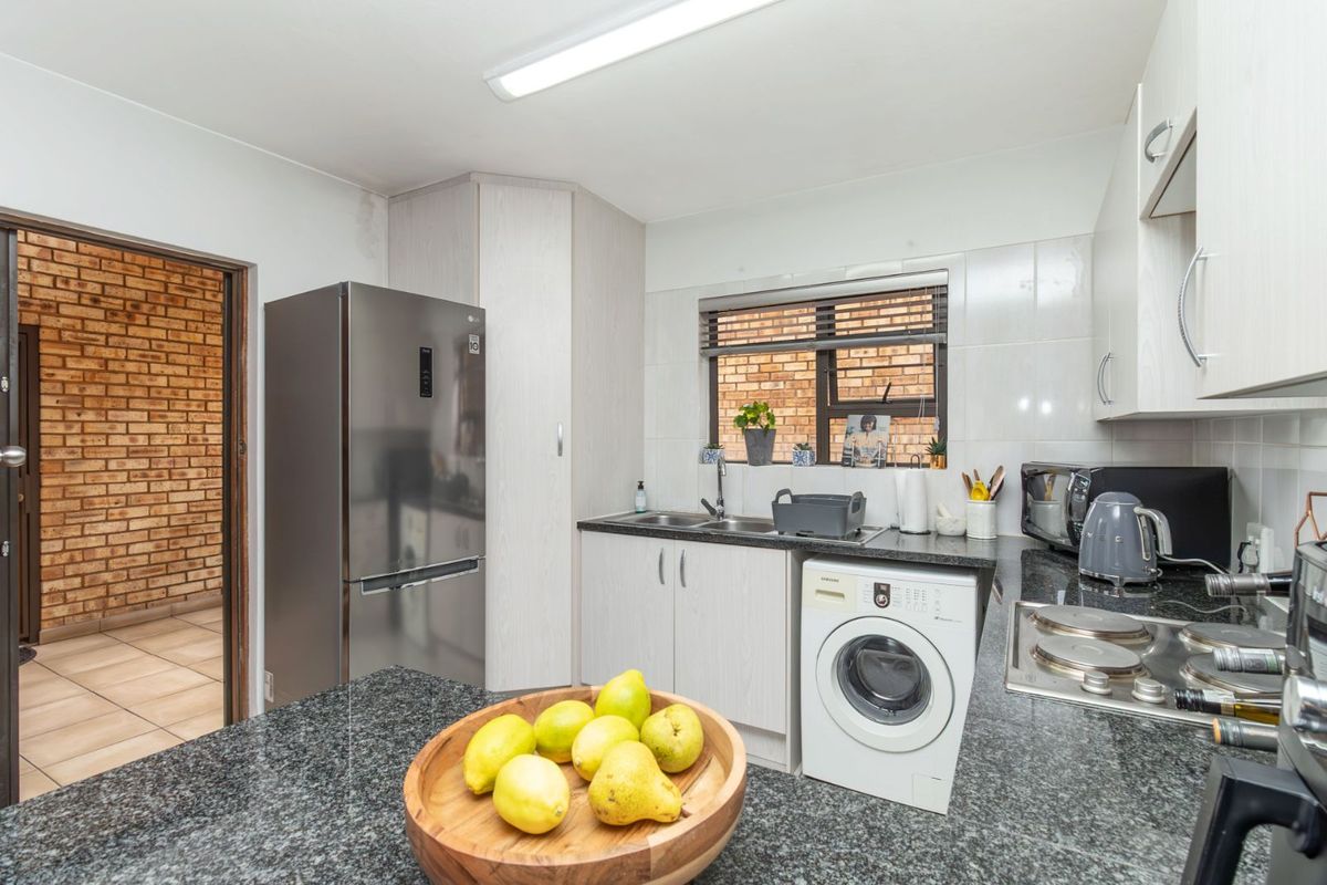 Compact kitchen featuring granite countertops, built-in cabinetry, integrated washing machine, and a stainless steel sink with a view of the adjacent brick-walled room.