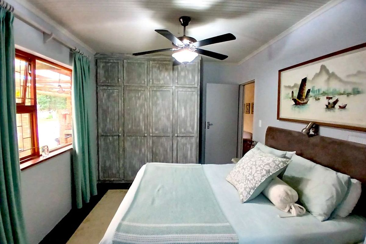 A well-maintained bedroom featuring built-in wooden cabinetry, a ceiling fan, and large windows that provide natural light.