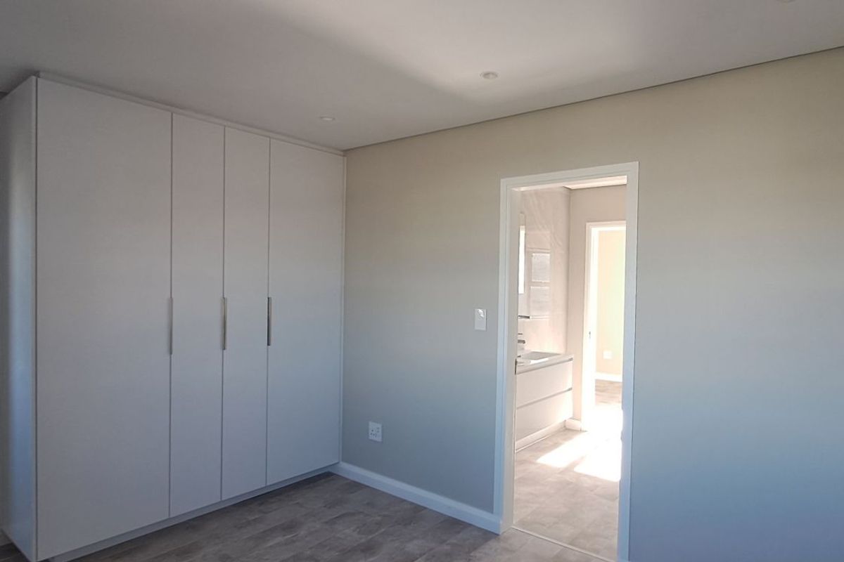 A bright bedroom featuring built-in floor-to-ceiling wardrobes and direct access to an en-suite bathroom with modern finishes.