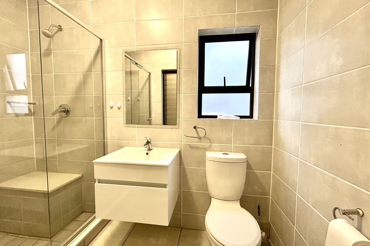 Modern bathroom featuring a glass-enclosed shower, wall-mounted vanity with basin, and a toilet, finished with neutral floor-to-ceiling wall tiles.