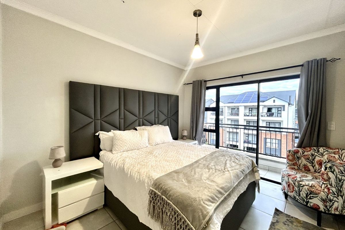 A well-lit bedroom featuring tiled flooring, a large sliding glass door leading to a private balcony, and a modern pendant light fixture.