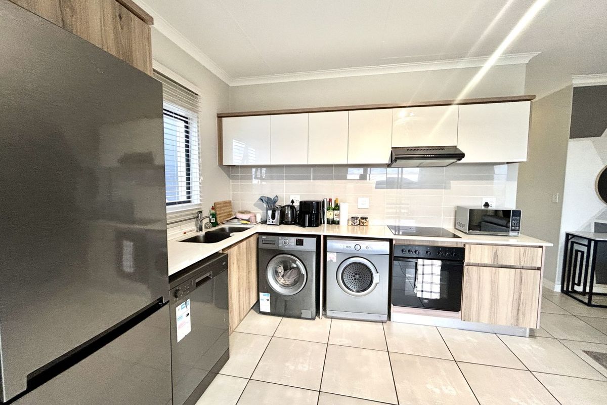 Modern kitchen featuring light wood-grain cabinetry, white high-gloss upper cabinets, tiled backsplash, integrated oven, hob, extractor fan, and dedicated laundry appliance spaces.