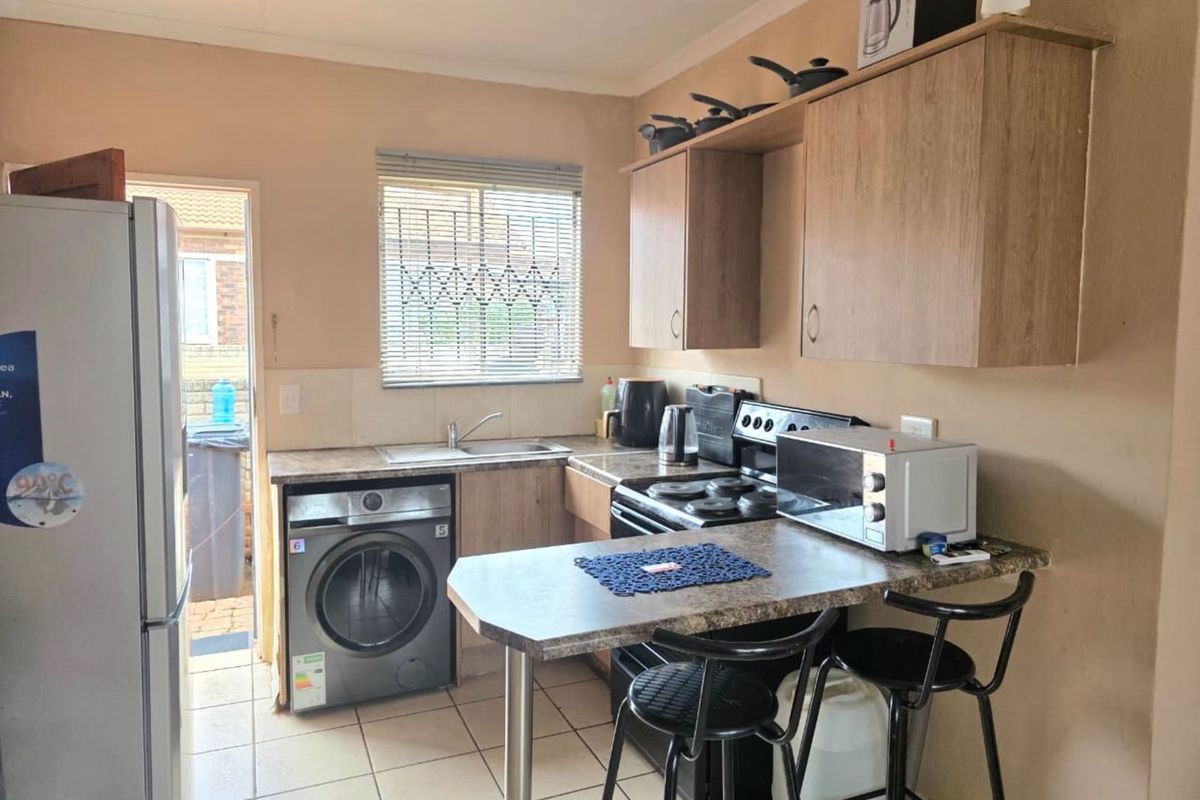 Compact kitchen featuring laminate countertops, built-in cabinetry, tiled flooring, and a dedicated space for laundry appliances with direct access to the exterior.
