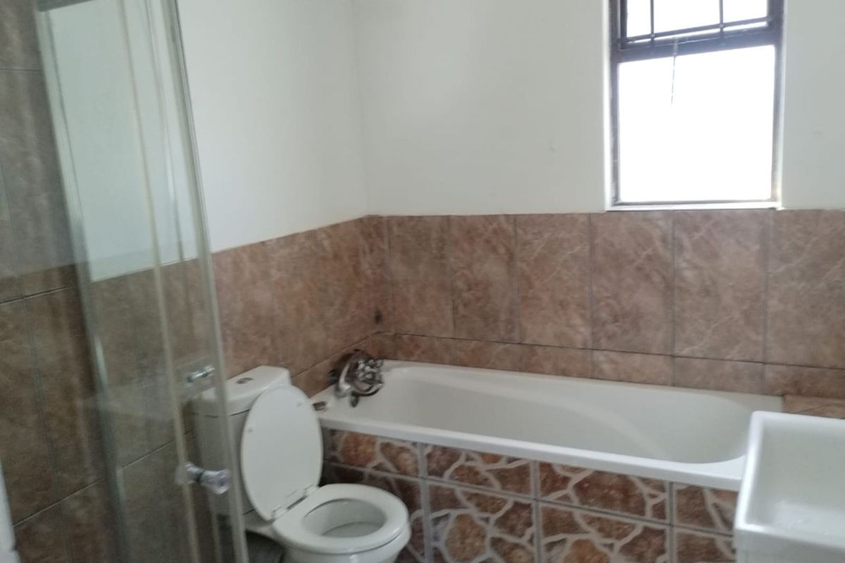 A functional bathroom featuring a built-in bathtub with decorative tiling, a separate glass-enclosed shower, and a standard toilet.