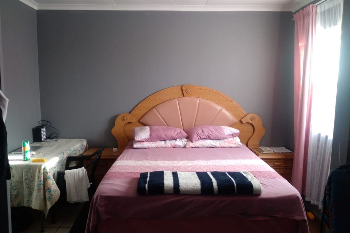 A bedroom featuring grey painted walls, tiled flooring, and a window with curtains.