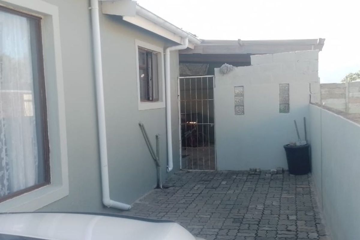 A rear exterior view of the property featuring a paved courtyard area, security gate, and perimeter walling.