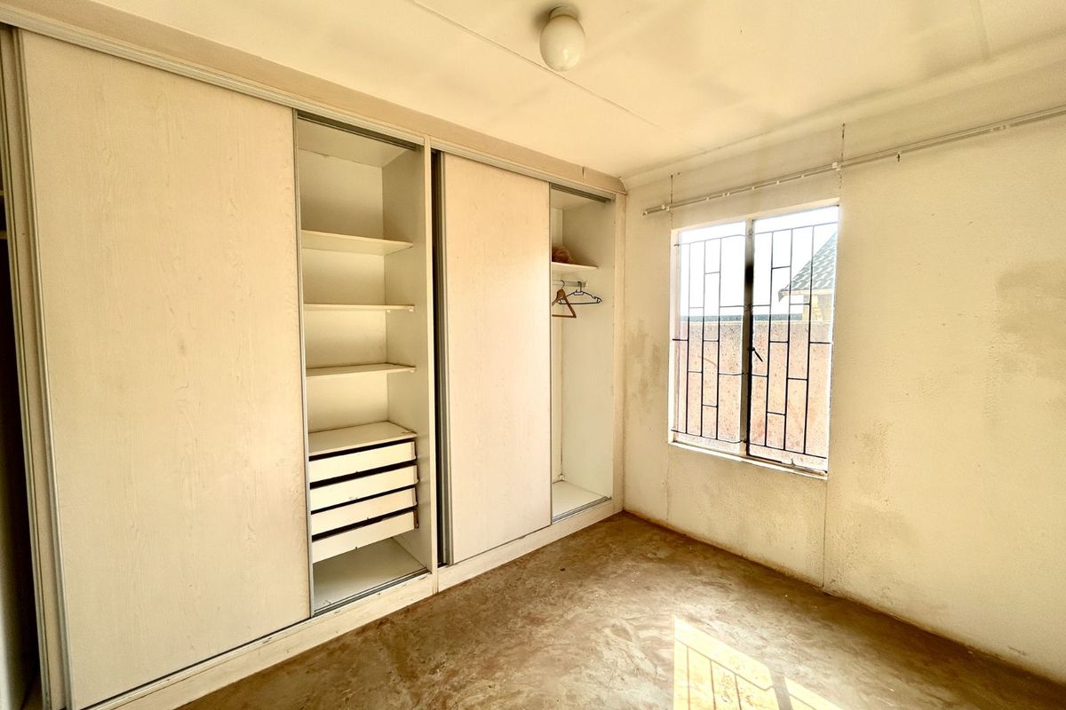 A vacant bedroom featuring built-in sliding door cupboards with shelving and drawers, a window with security bars, and a concrete floor.
