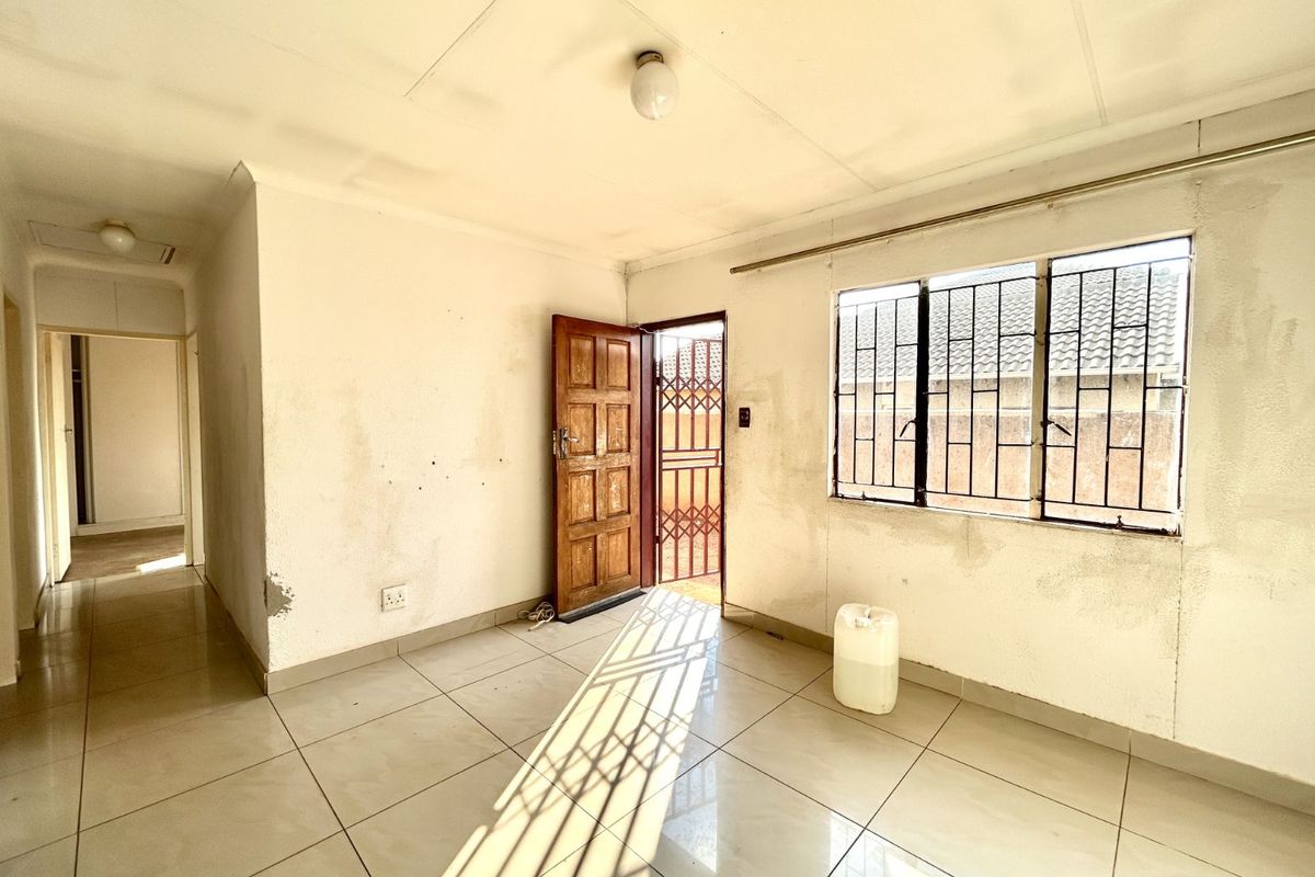 A vacant living area featuring tiled flooring, security bars on windows, and a wooden entrance door leading to an exterior security gate.