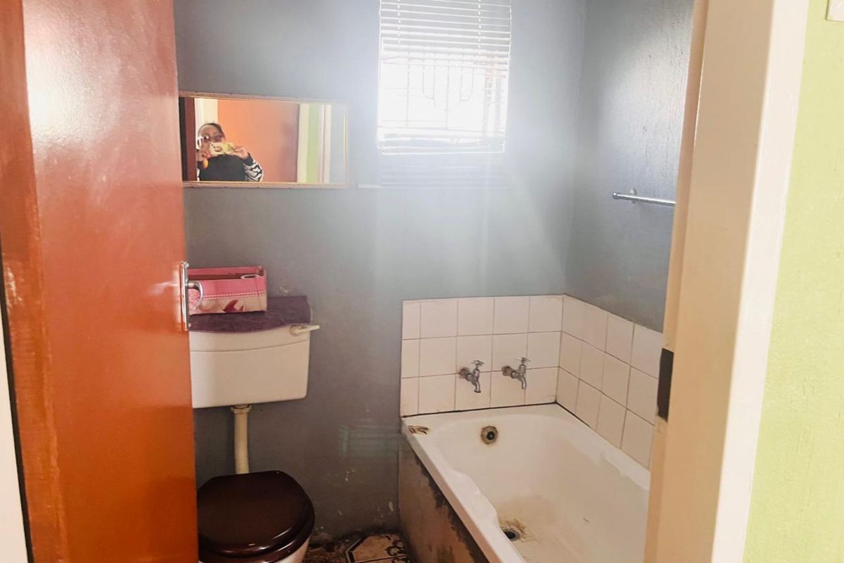 A compact bathroom featuring a standard bathtub with tiled splashback, a toilet, and a window with blinds.