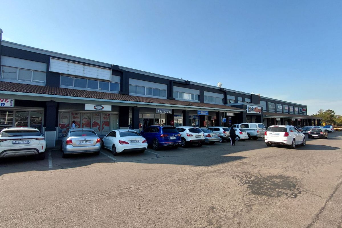 Exterior view of a retail strip mall featuring multiple storefronts with signage, covered walkways, and an adjacent asphalt parking area.