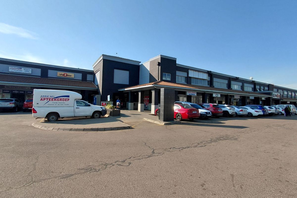 Exterior view of a retail shopping center featuring a paved parking lot, covered walkways, and multiple storefronts with signage.
