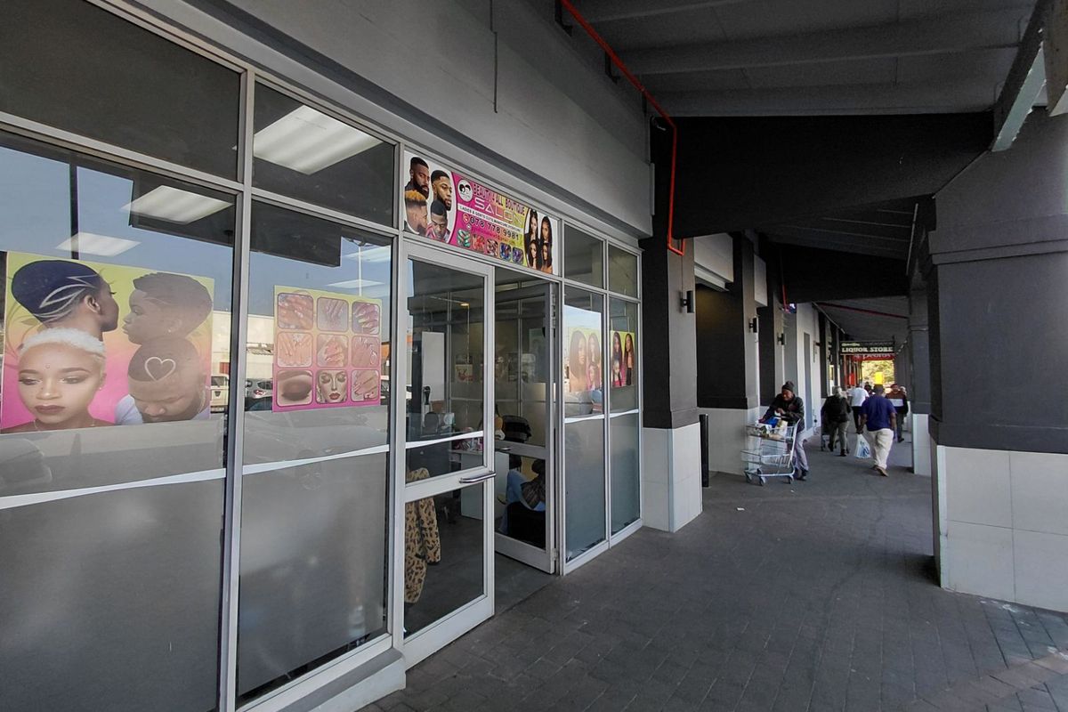 Front facade of a retail salon unit featuring large glass display windows and a glass entrance door, situated under a covered walkway.