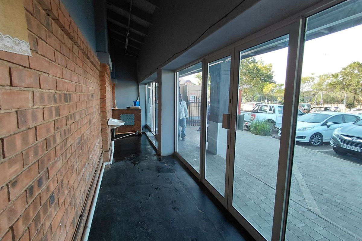 Interior retail space featuring an exposed brick wall, large glass storefront windows, and a concrete floor with a small wall-mounted basin.