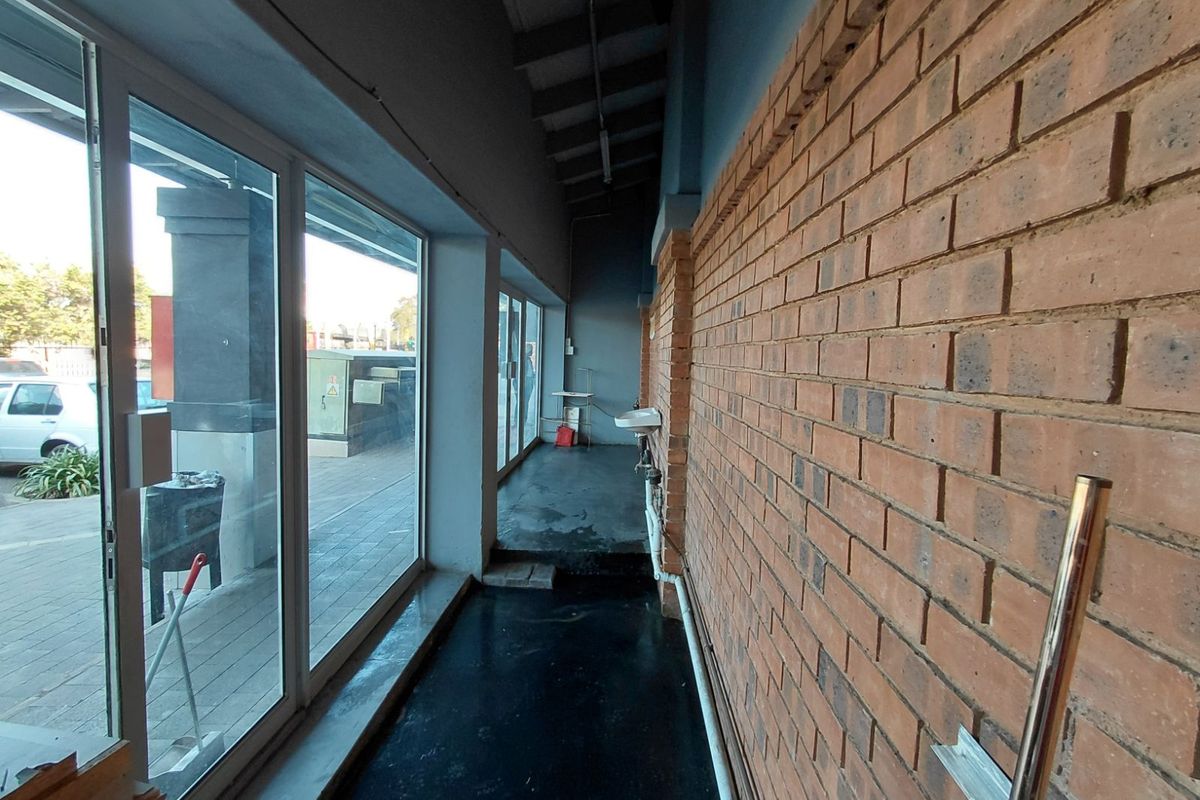 A narrow utility corridor featuring exposed brickwork, large glass storefront windows, and a wall-mounted basin.
