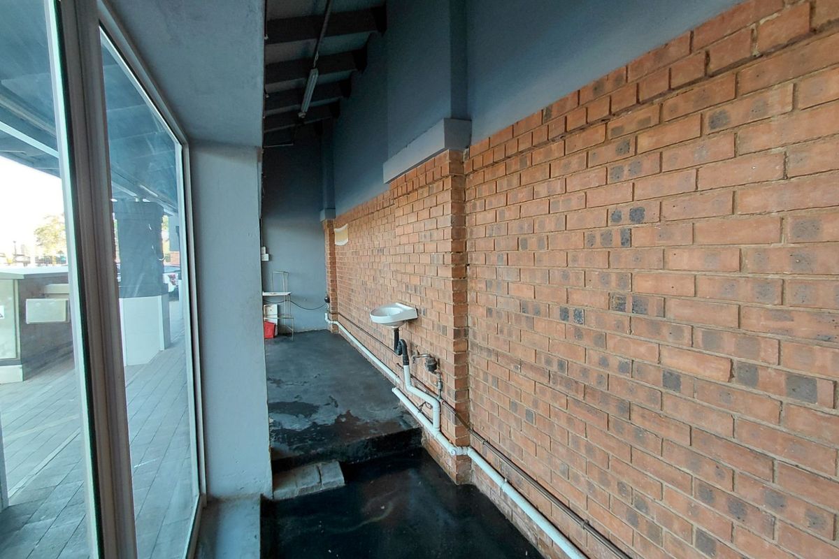 A narrow utility corridor featuring an exposed brick wall, a small wall-mounted basin, and large glass windows overlooking the exterior area.
