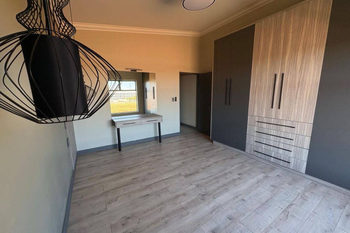 A modern bedroom featuring built-in floor-to-ceiling cabinetry with a two-tone wood and charcoal finish, light wood-look flooring, and a built-in vanity area.