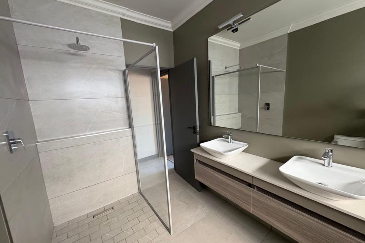 Modern bathroom featuring a spacious walk-in shower with glass enclosure, double vanity with vessel sinks, and large wall-mounted mirror.
