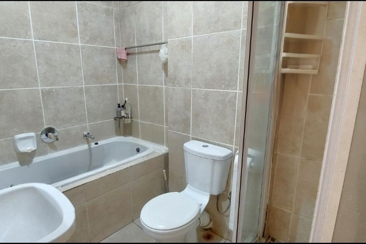 A functional bathroom featuring a built-in bathtub, separate shower enclosure, toilet, and pedestal basin with neutral wall tiling.