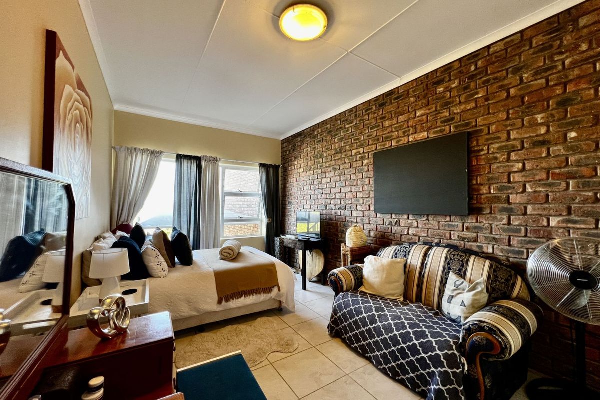 A bedroom featuring a prominent exposed brick feature wall, tiled flooring, and large windows allowing natural light.