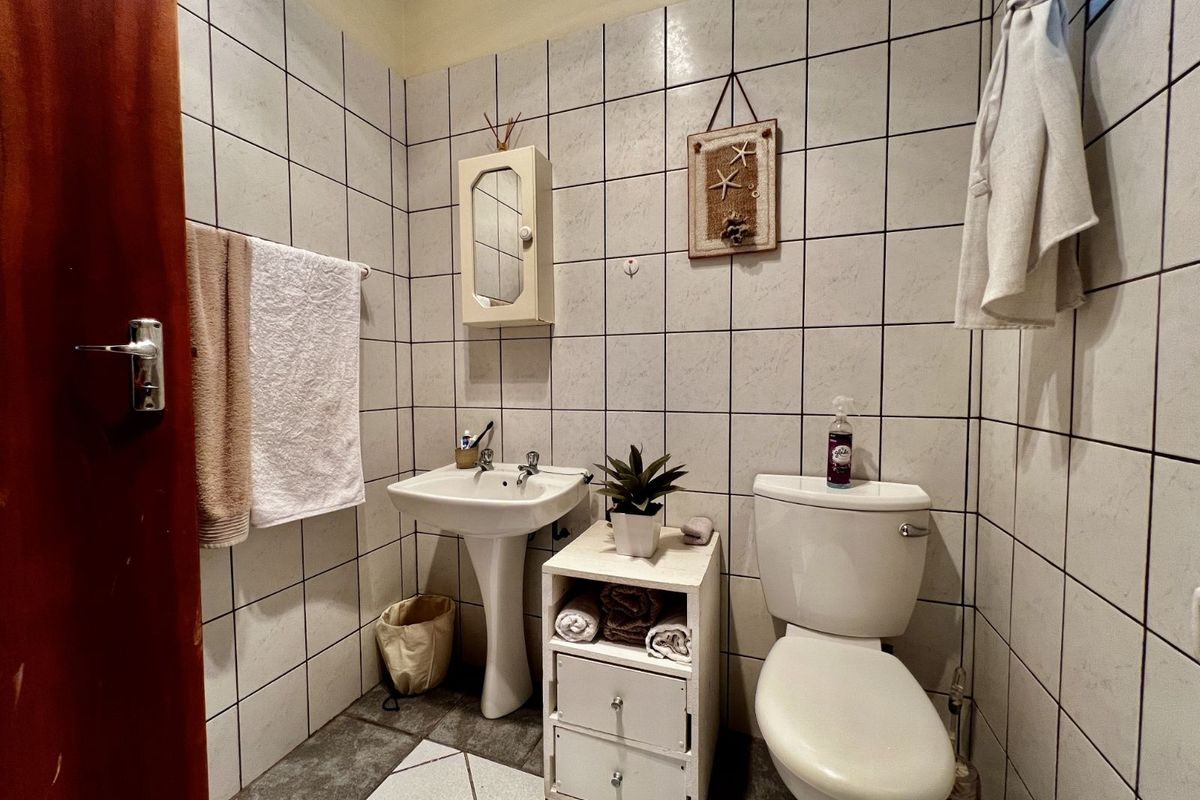 A compact bathroom featuring a pedestal basin, a standard toilet, and full-height wall tiling.