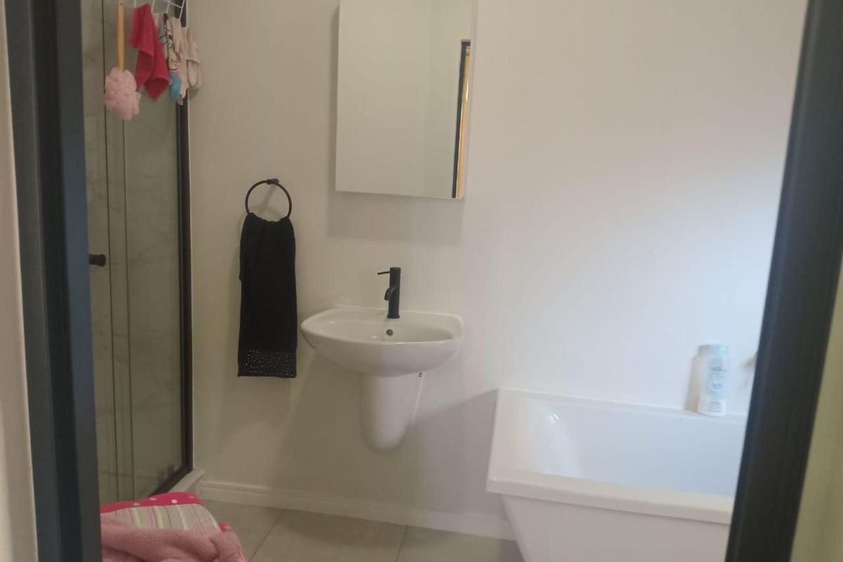 A functional bathroom featuring a wall-mounted pedestal basin with a modern black tap, a separate shower enclosure, and a white bathtub.