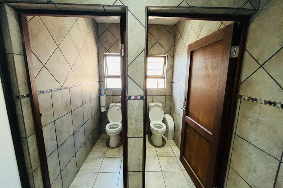 Two separate restroom cubicles featuring tiled walls and floors, each equipped with a standard toilet and window for natural ventilation.