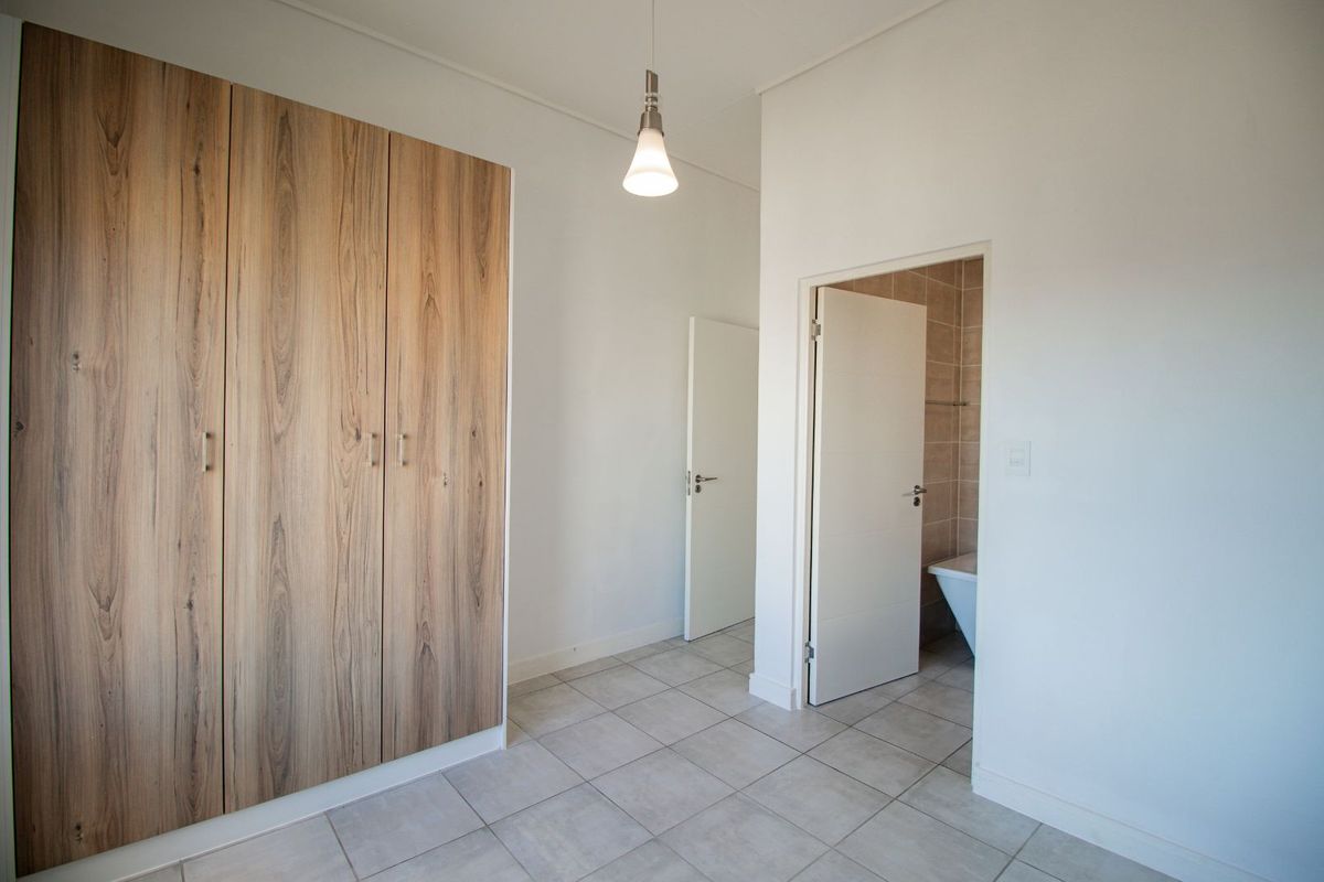A bright bedroom featuring built-in wood-grain wardrobes, tiled flooring, and direct access to an en-suite bathroom.