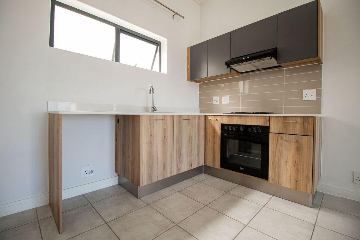 Modern kitchen featuring wood-grain cabinetry, stone countertops, built-in oven, hob, and extractor fan with tiled flooring and neutral finishes.