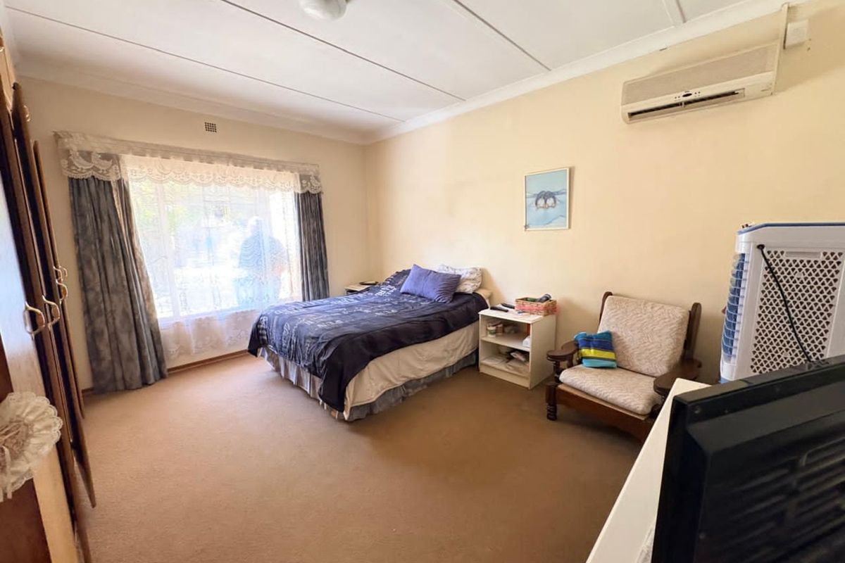 Spacious bedroom featuring a wall-mounted air conditioning unit, large window with curtains, and neutral wall finishes.