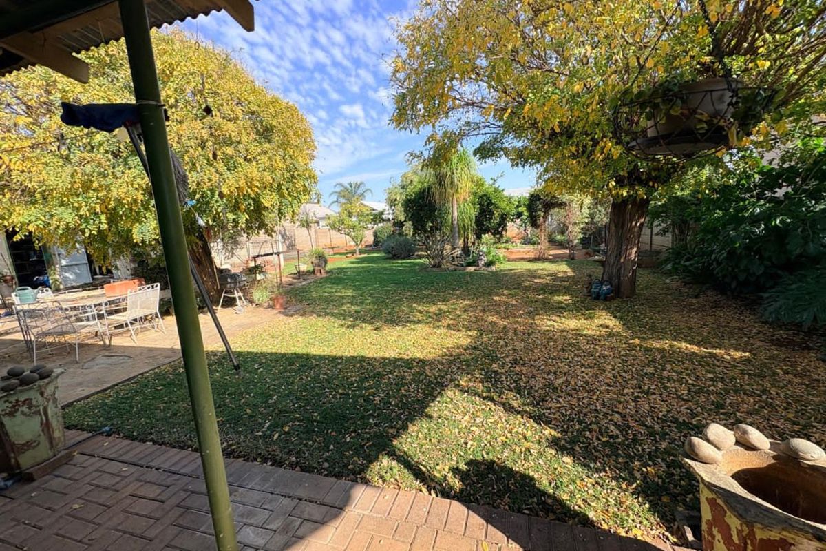 A spacious rear garden featuring a paved patio area, mature trees, and a well-maintained lawn, providing a peaceful outdoor setting.