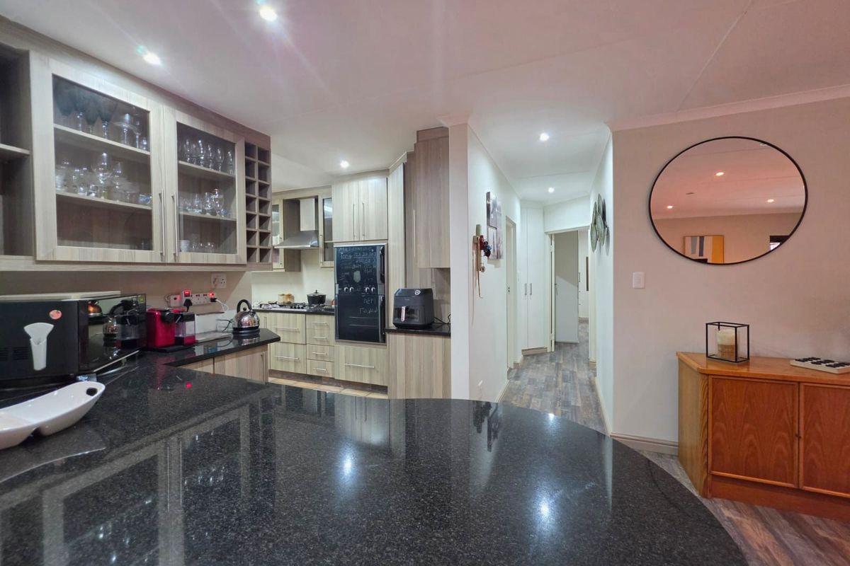 Modern kitchen featuring granite countertops, ample cabinetry, and integrated appliances, flowing into a bright hallway with recessed lighting.