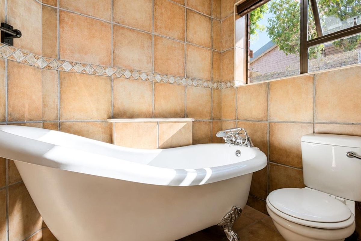 A bathroom featuring a classic clawfoot bathtub and a standard toilet, finished with warm-toned ceramic wall tiles and a window for natural light.