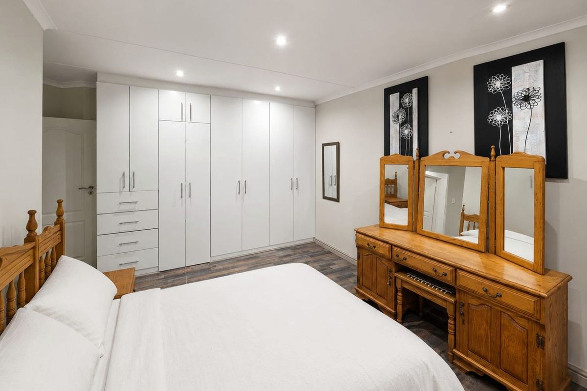 A well-maintained bedroom featuring extensive floor-to-ceiling built-in white cabinetry, recessed downlighting, and modern wood-look flooring.