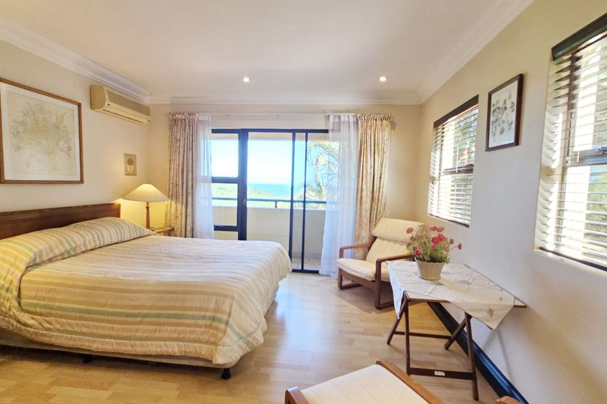 Spacious bedroom featuring light wood flooring, recessed lighting, a wall-mounted air conditioning unit, and sliding glass doors opening to a private balcony with ocean views.