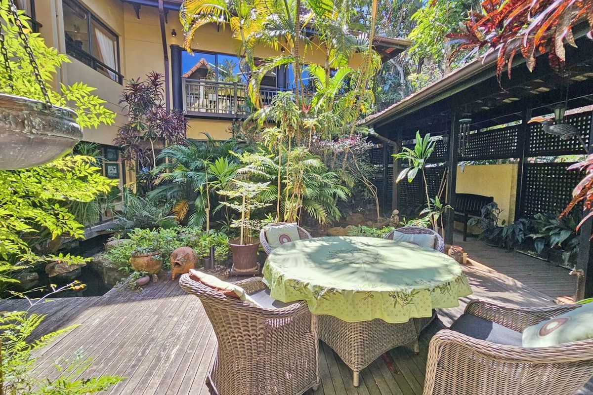 A lush, tropical-style rear courtyard featuring timber decking, a covered patio area, and established garden landscaping adjacent to the main residence.
